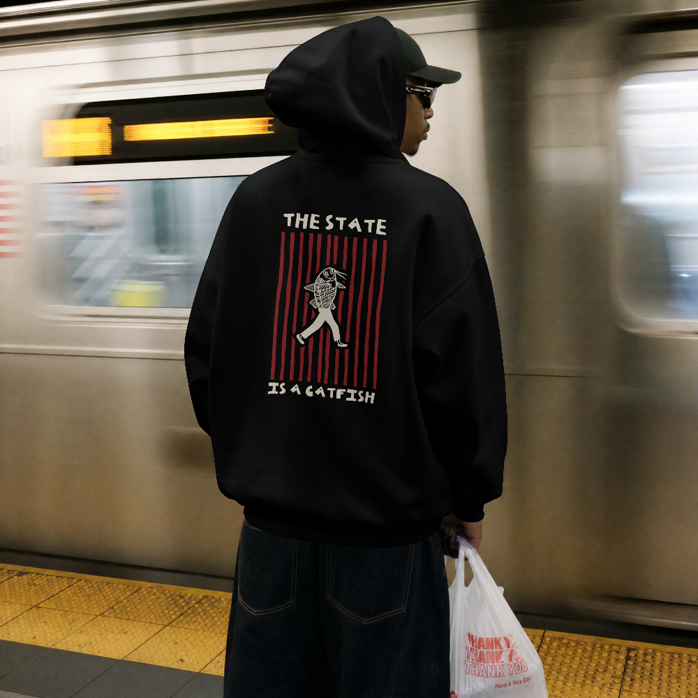 The State is a Catfish hoodie in black worn by a model at a train station, back view with The State Is a Catfish graphic