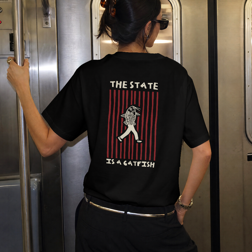 The State is a Catfish classic tee in black worn by a model on a train, back view with The State Is a Catfish graphic
